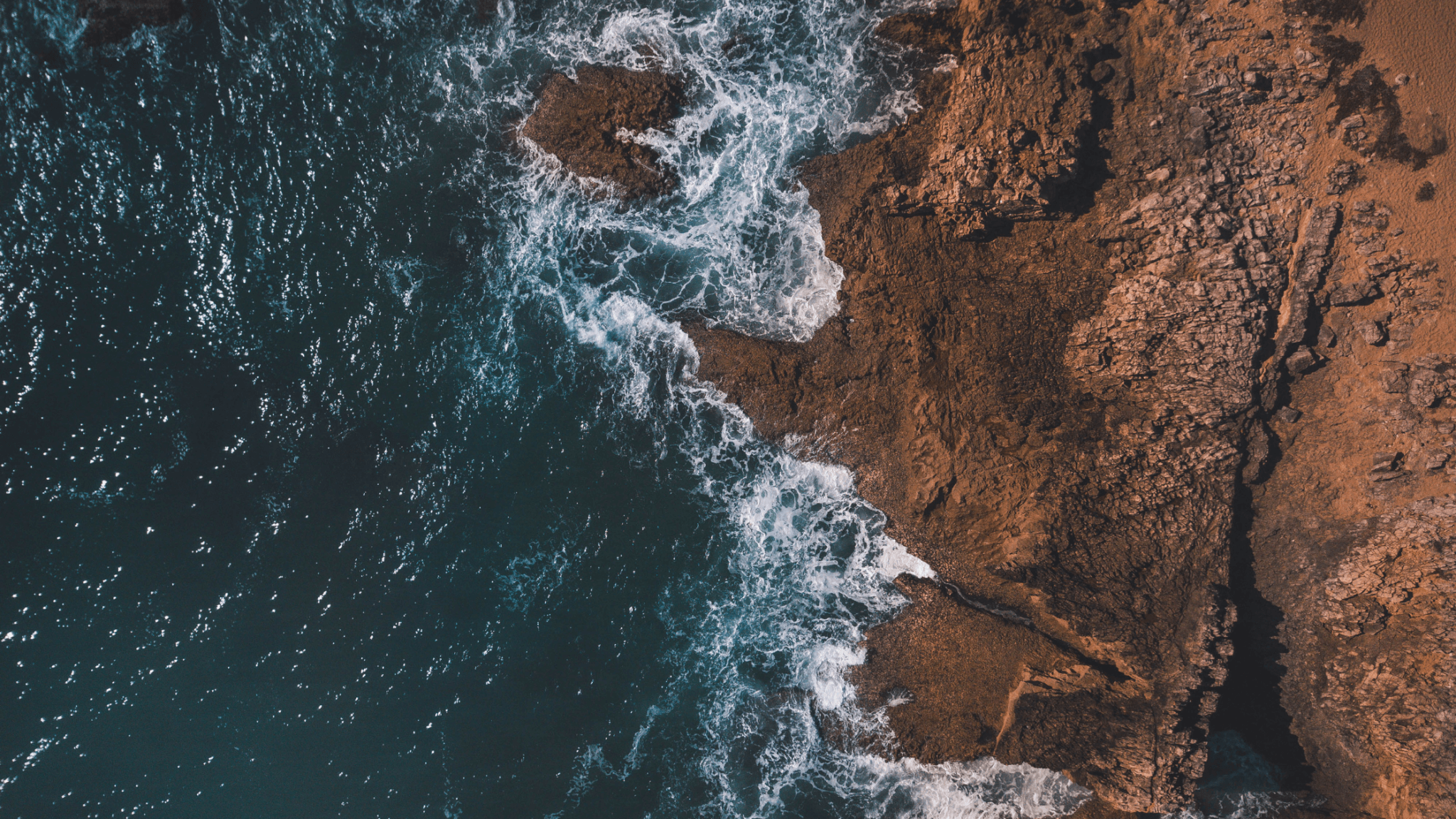 Overhead shot of waves crashing on the shore, forming an artistic organic pattern